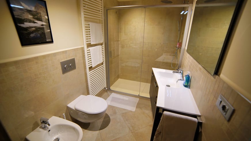 Modernes Badezimmer in der Pensione Ceaglio mit beigen Fliesen, bodengleicher Dusche und Holzunterschrank.