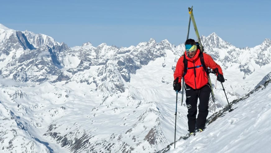 Mit Tourenskiern und Skistöcken steigt Bergführer Matthias Hahn in roter Winterjacke einen schneebedeckten Hang hinauf.