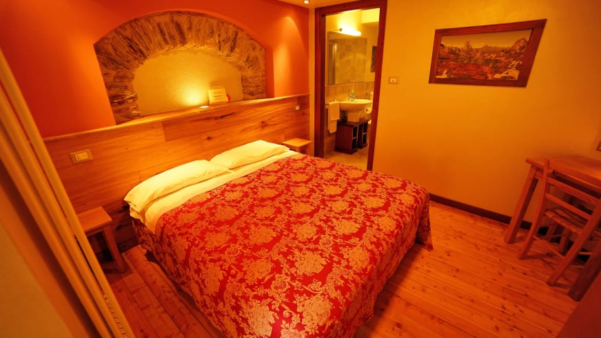 Zimmer Mulo im Hotel Pensione Ceaglio zeigt ein Doppelbett vor Holzverkleidung mit integriertem Steinbogen als Betthaupt.
