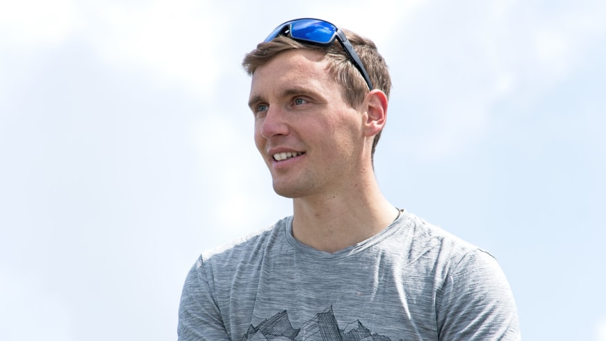 Bergführer Matthias Hahn trägt graues T-Shirt mit Bergmotiv und blaue verspiegelte Sonnenbrille vor weißem Hintergrund.