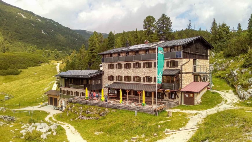 Luftaufnahme der Traunsteiner Hütte mit großer Sonnenterrasse und gelben Sonnenschirmen in alpiner Lage.