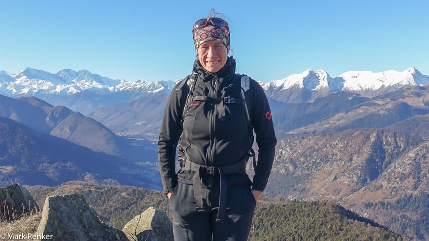 Bergwanderführerin Corry Heiland lächelt auf einem Berggipfel vor weitem Alpenpanorama mit schneebedeckten Gipfeln.
