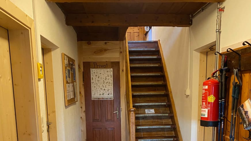 Eingangsbereich der Richterhütte mit zentraler Holztreppe zum Obergeschoss und Wandhaken.