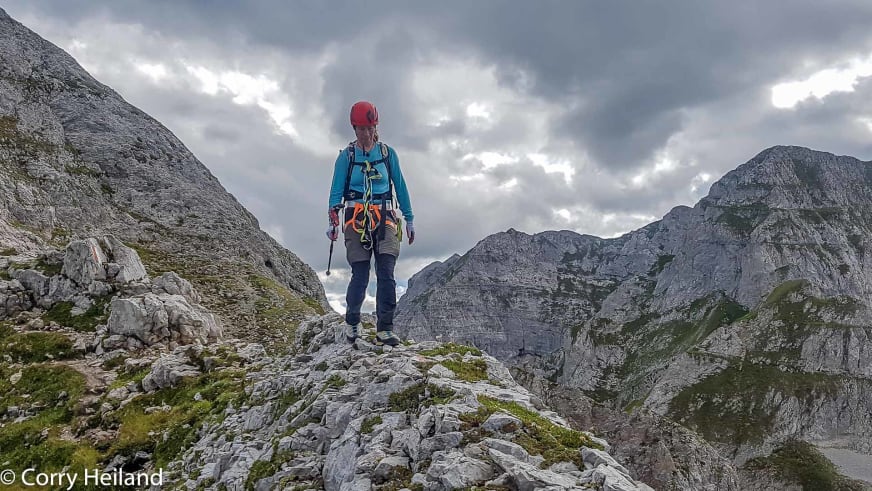 In türkisfarbenem Oberteil und rotem Helm steht Bergwanderführerin Corry Heiland auf Felsplateau in zerklüfteter Kalksteinlandschaft.