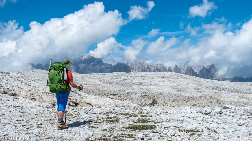 Mit grünem Rucksack und Wanderstöcken wandert Bergwanderführer Mark Renker über ein kahles Kalksteinplateau.