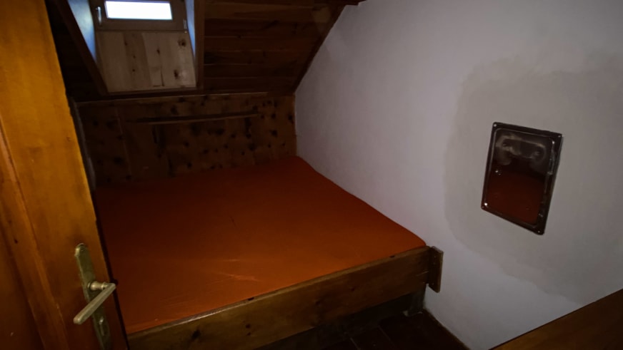 Einfaches Einzelbett der Richterhütte unter Dachschräge mit Holzrahmen und Dachfenster.