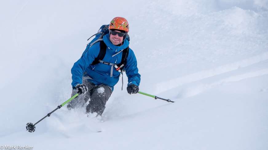 In tiefem Pulverschnee fährt Bergwanderführer Mark Renker mit orangenem Helm und blauer Winterjacke ab.