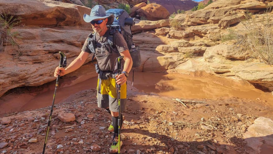 Durch rötliche Sandsteinlandschaft wandert Bergwanderführer Mark Renker mit hellem Hut und Wanderstöcken.