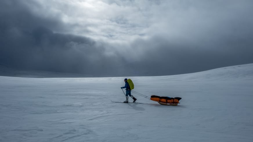 Über weite Schneelandschaft zieht Bergwanderführer Mark Renker auf Skiern einen orangefarbenen Pulkaschlitten.