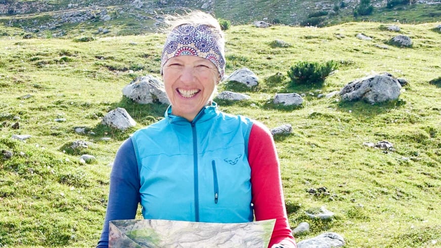 Bergwanderführerin Ruth Zeller hält eine topografische Karte und trägt türkisfarbene Softshell-Weste in alpiner Landschaft.