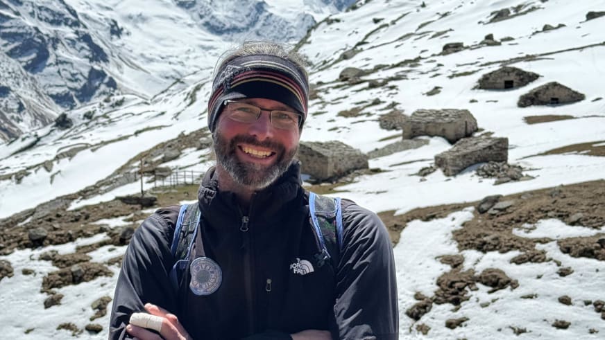 Bergführer Thomas Scherzer mit Brille und gestreiftem Stirnband lächelt vor verschneiter Berglandschaft.