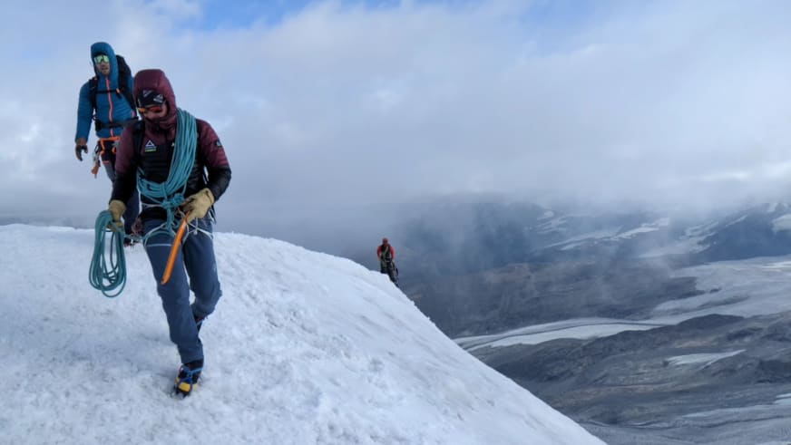 Auf schneebedecktem Bergrücken führt Bergführer Thomas Scherzer in weinroter Jacke mit Steigeisen und Eispickel.