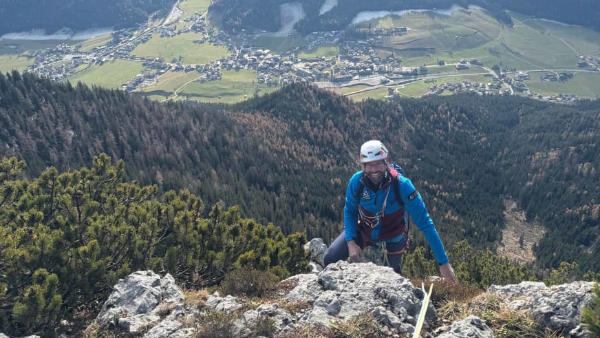 Thomas Scherzer klettert in blauer Jacke am Kalksteinabbruch mit weitem Talblick als Bergführer.