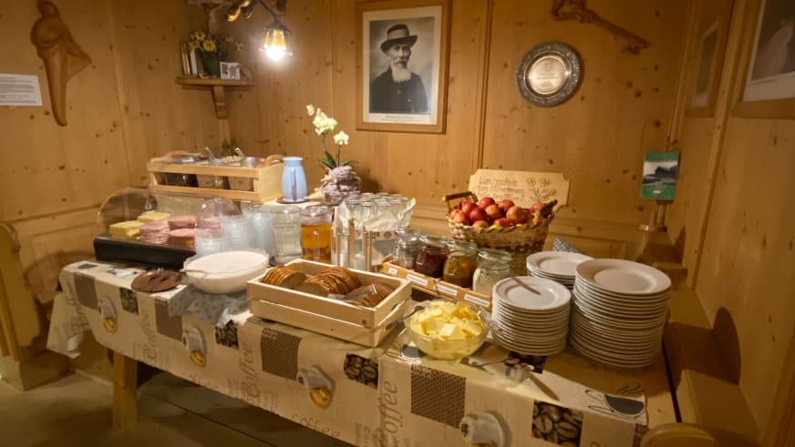 Frühstücksbuffet in der Zittauer Hütte mit gestapelten Tellern, Brotkorb, Marmelade und frischem Obst.