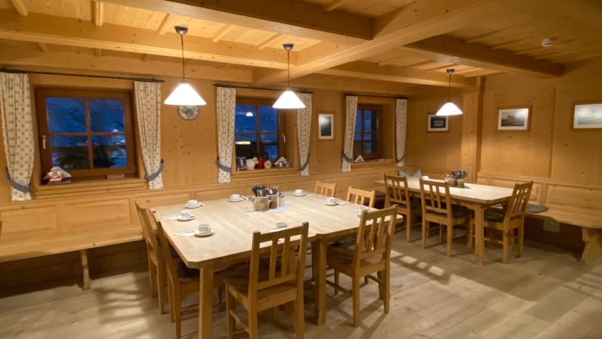 Gaststube der Zittauer Hütte mit zwei gedeckten Holztischen unter Holzbalkendecke und warmer Abendbeleuchtung.