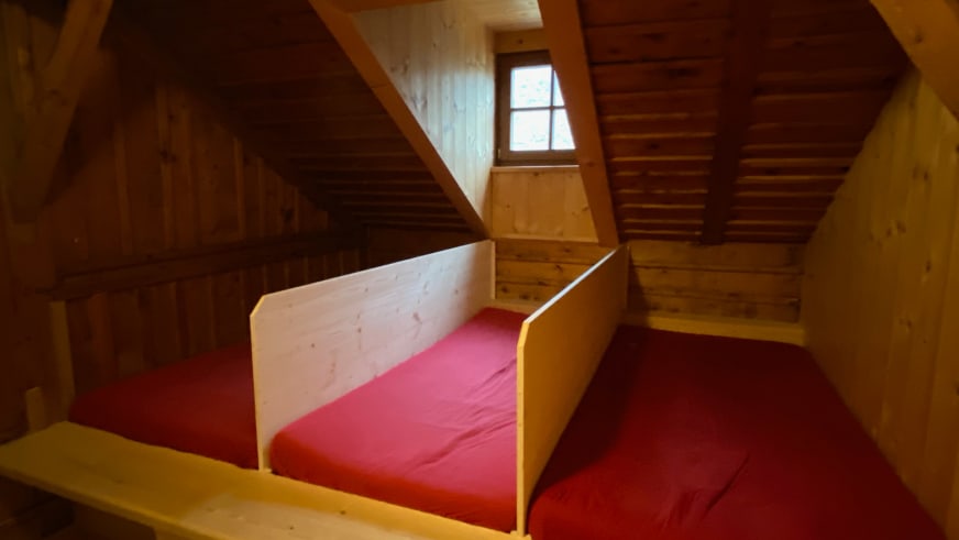 Schlafraum der Zittauer Hütte mit zwei Einzelbetten unter der Dachschräge aus naturbelassenem Holz.