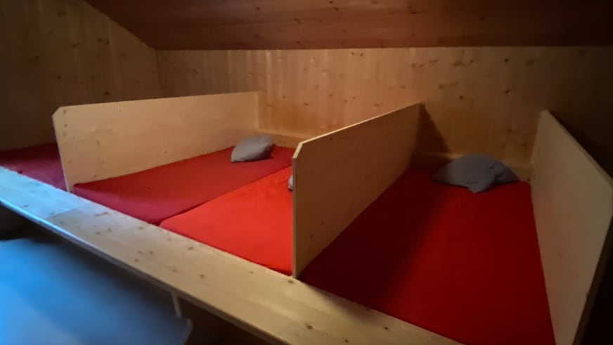 Schlaflager der Zittauer Hütte mit zwei Einzelbetten, roten Matratzen und sichtbaren Holzbalken unter Dachschräge.