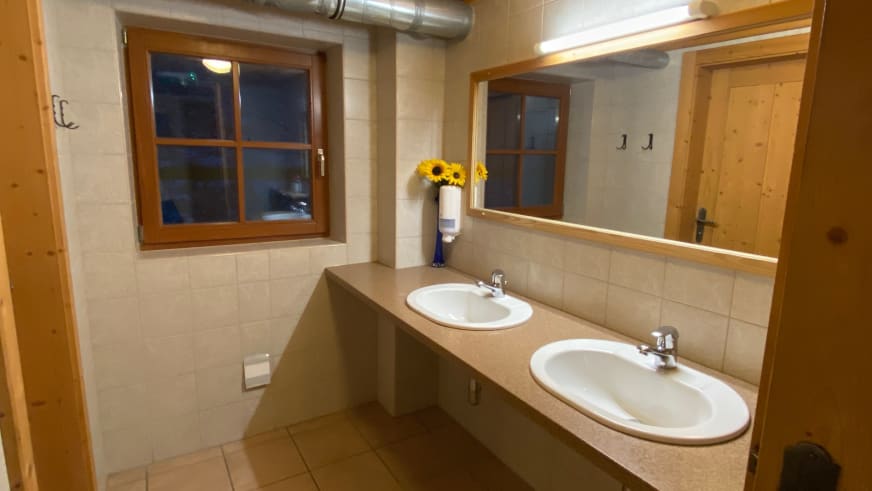Badezimmer der Zittauer Hütte mit zwei Waschbecken, Steinarbeitsplatte und Fenster zur Abenddämmerung.