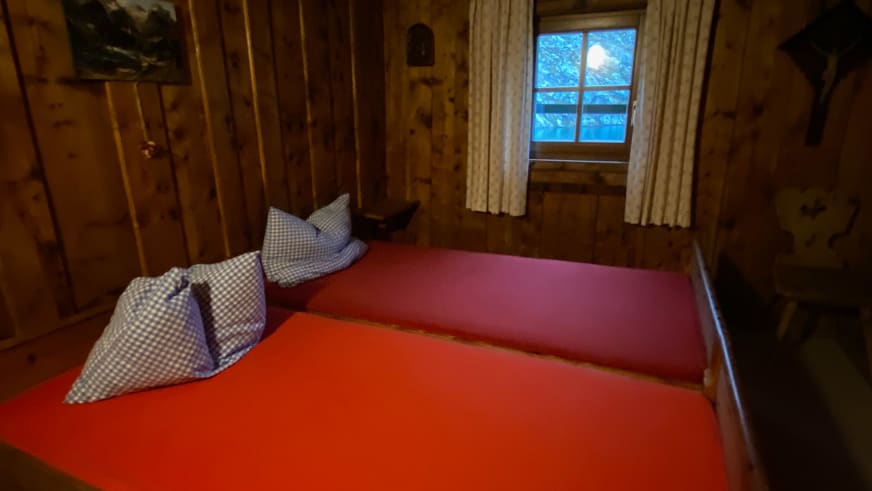 Eingebaute Bettnische in der Zittauer Hütte mit roter Matratze und karierter Bettwäsche im Alpendesign.