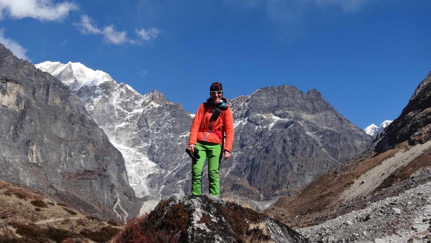 Bergwanderführerin Elisabeth Götzinger steht in orangener Jacke auf einem Felsbrocken im Hochtal.