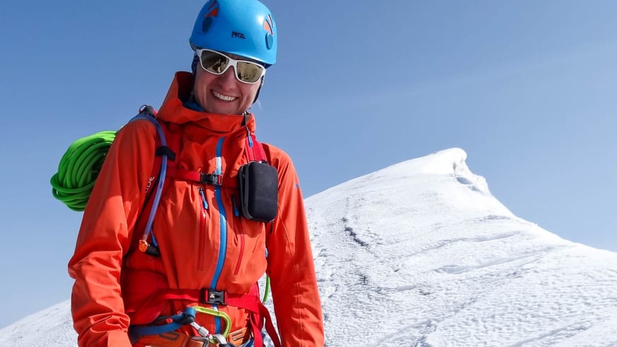Bergwanderführerin Elisabeth Götzinger mit blauem Kletterhelm und Kletterausrüstung auf verschneitem Gipfel.