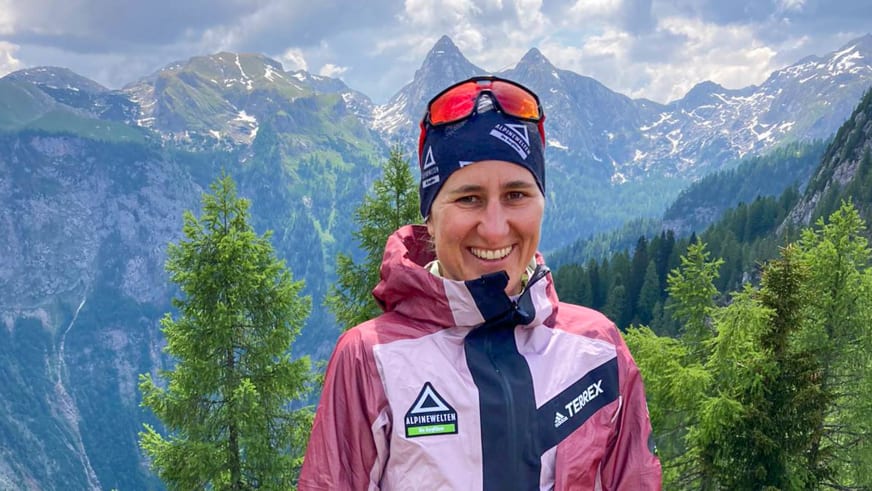 Portrait von Bergwanderführerin Elisabeth Götzinger mit rosa Outdoorjacke vor schneebedeckten Gipfeln.