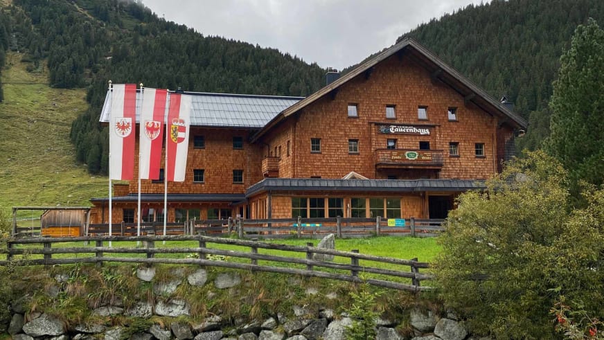 Außenansicht des Krimmler Tauernhauses mit Holzschindelfassade und überdachter Terrasse.