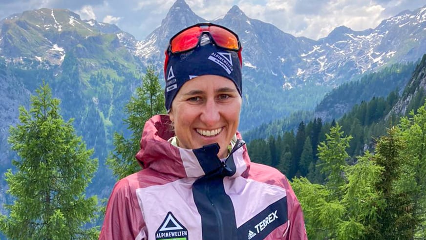 Bergwanderführerin Elisabeth Götzinger mit Skibrille auf der Stirn vor bewaldeten Berghängen.