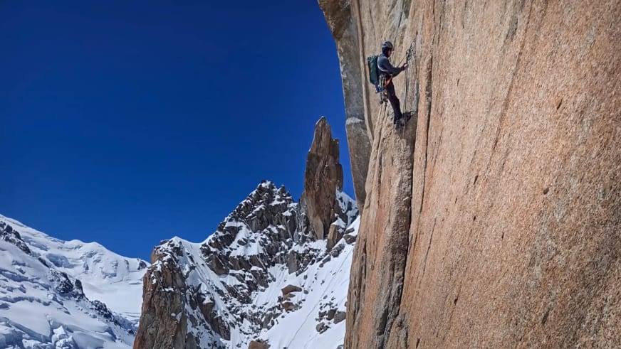 Alpines Klettern mit Bergführer Christian Färber an steiler Felswand vor schneebedeckten Gipfeln im Hintergrund.