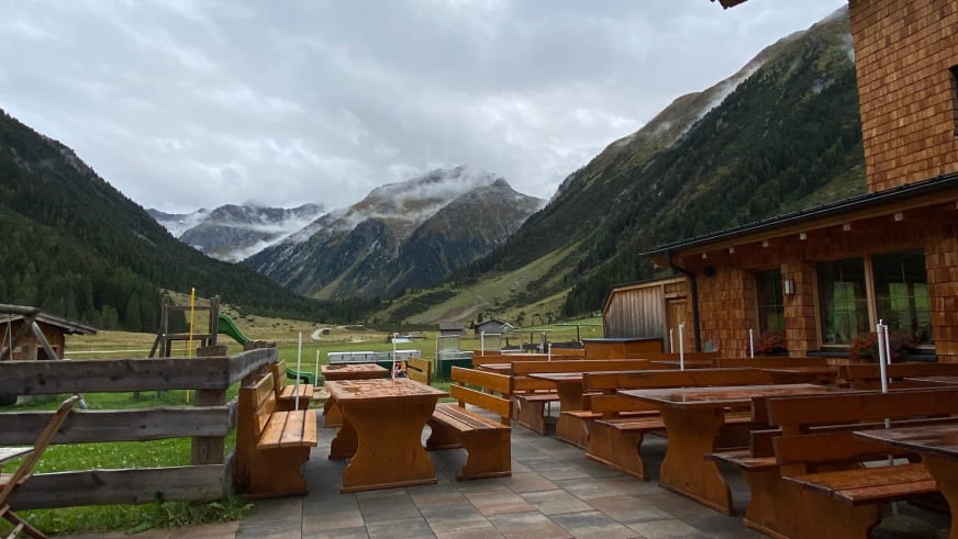 Holzterrasse mit traditionellen Almtischen vor dem Krimmler Tauernhaus bei bewölktem Himmel.