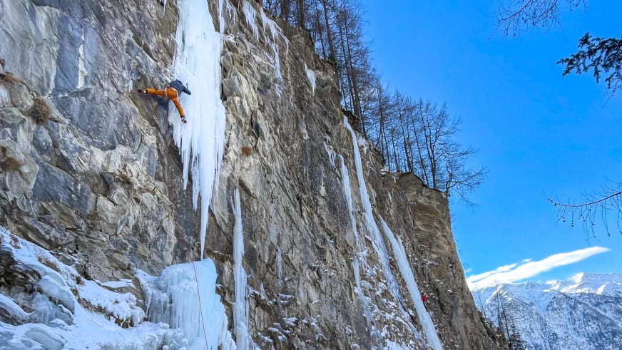 Bergführer Christian Färber klettert in orangefarbener Winterkleidung an vereister Felswand mit langen Eiszapfen.