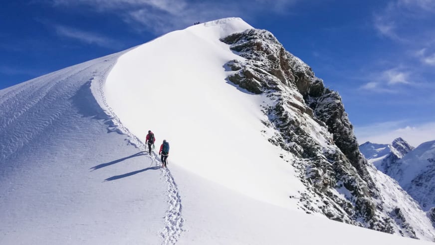 Bergführer Christian Färber steigt mit Begleitung auf schmalem Schneegrat in Richtung Gipfel mit Firnkappe auf.