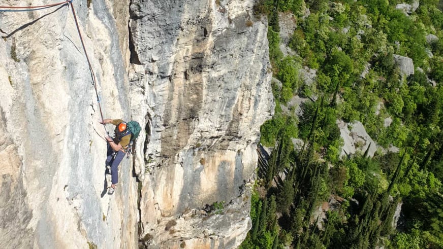 Bergführer Christian Färber klettert mit orangem Helm an steiler Kalksteinwand über tiefer grüner Schlucht.