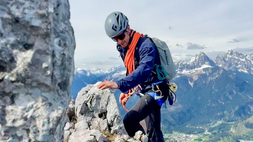 Bergführer Christian Färber sitzt in vollständiger Kletterausrüstung auf Felsvorsprung mit Alpenpanorama im Hintergrund.