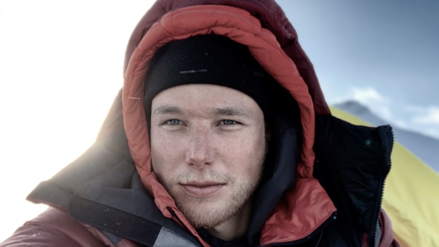 Bergwanderführer Jonas Haass trägt dicke Kapuze mit orangefarbenem Innenfutter vor schneebedeckten Bergen.
