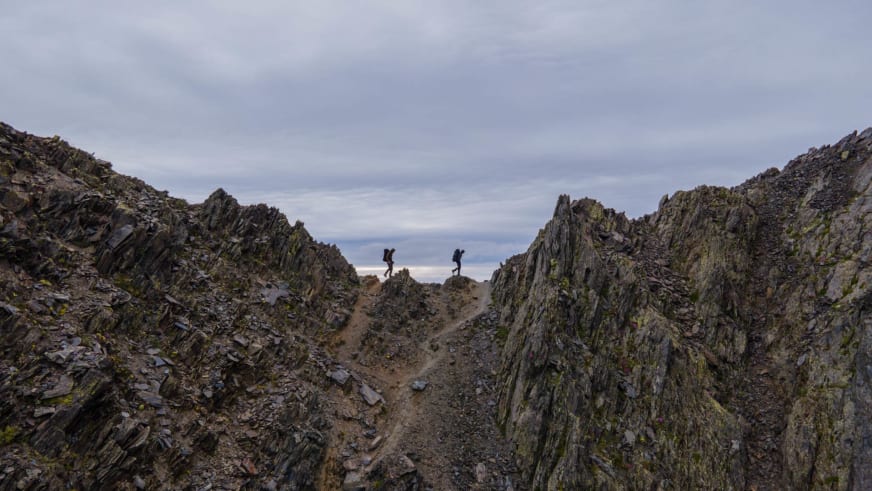 Bergwanderführer Jonas Haass mit zweiter Person wandert durch alpine Schlucht zwischen steilen Felswänden aus dunklem Gestein.