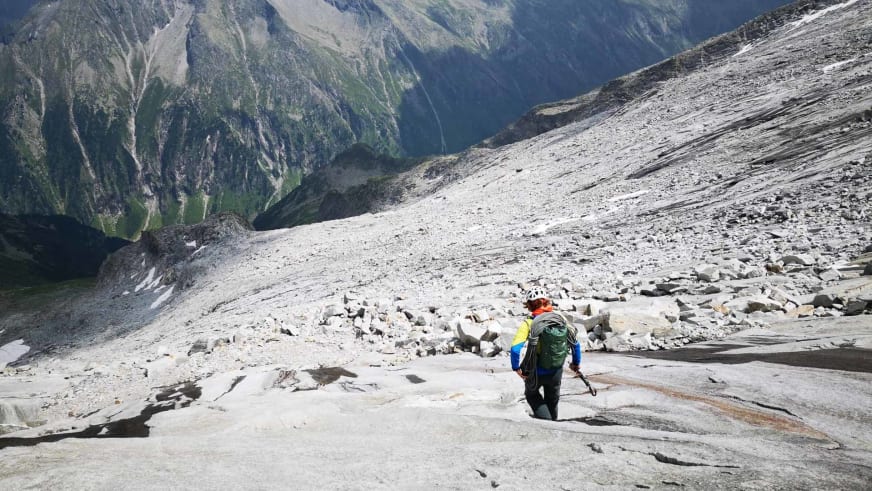 Bergführer Philipp Wagner mit weißem Helm und gelbblauer Jacke steigt über helle Felsplatten im Hochgebirge auf.