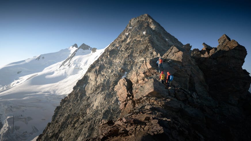 Auf einem schmalen Felsgrat bewegen sich drei Bergsteiger vorwärts, geführt von Bergführer Philipp Wagner.
