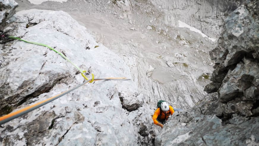An grauem Kalksteinfels klettert Bergführer Philipp Wagner in orangefarbener Jacke durch eine Verschneidung aufwärts.