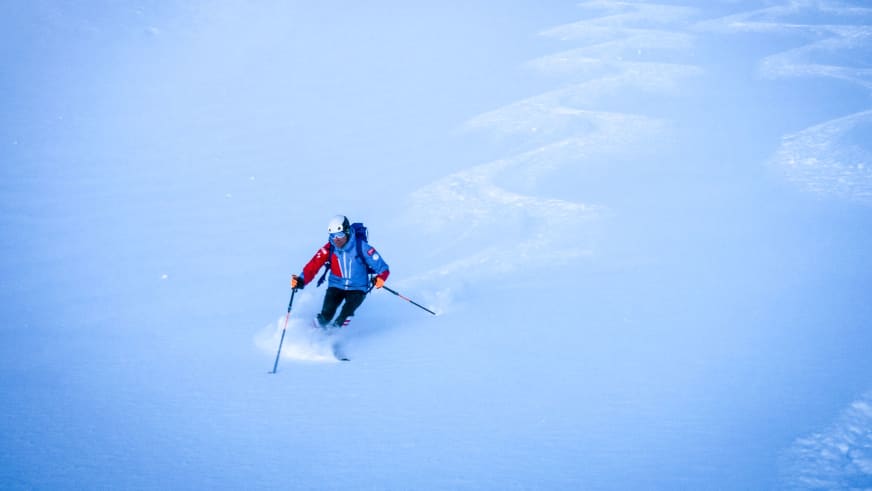 Bergführer Michael Eberharter fährt in roter Winterkleidung durch tiefen Pulverschnee, Schneewolke um die Skier.