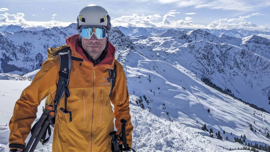 Bergführer Michael Eberharter trägt orange Arc'teryx Jacke und weißen Helm vor schneebedeckten Bergen.
