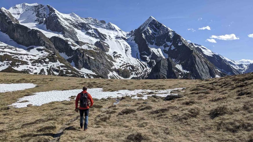 In roter Jacke wandert Bergführer Michael Eberharter über braune Almfläche mit Schneeflecken Richtung Bergkette.