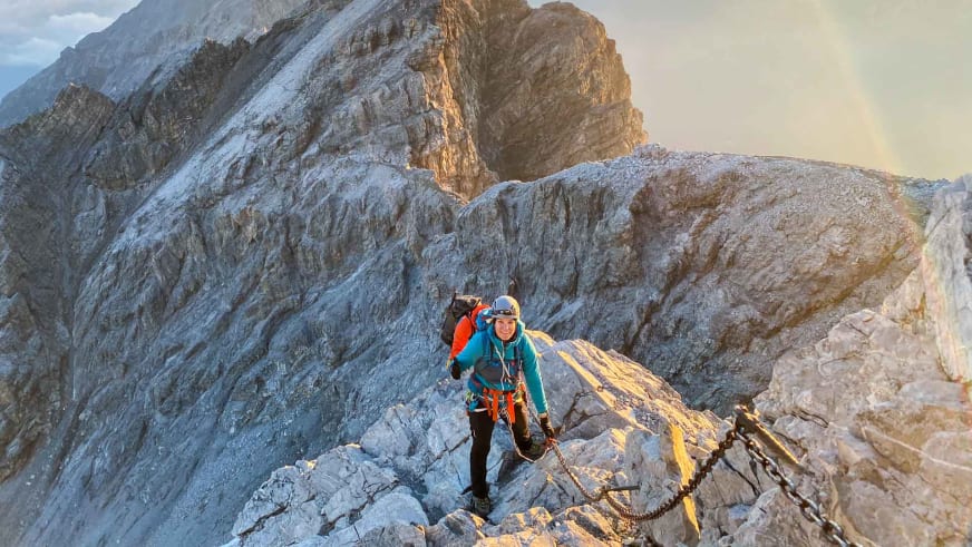 Am Klettersteig bewegt sich Bergwanderführerin Tatjana Reichert mit weißem Helm durch Kalksteingelände mit Eisenkette.