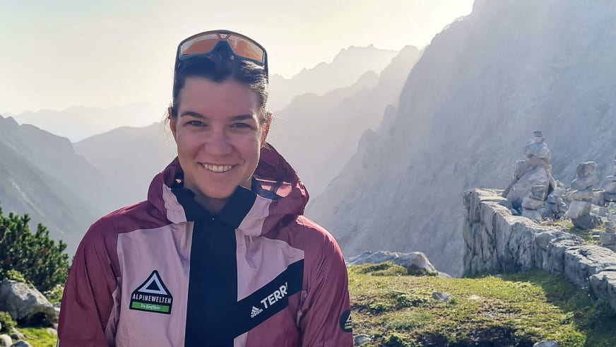 Portrait von Bergwanderführerin Tatjana Reichert in mehrfarbiger Outdoorjacke vor Gebirgslandschaft mit Steinformationen.