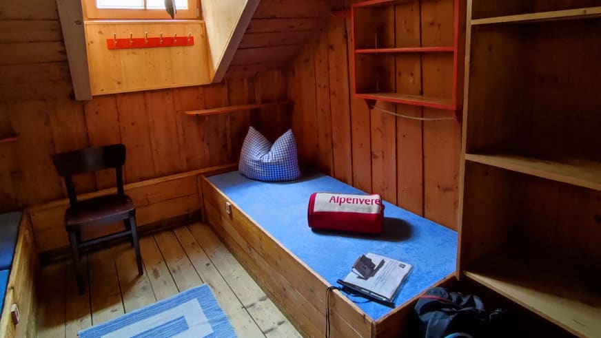 Einzelbett im Holzzimmer der Kaunergrathütte mit Alpenverein-Handtuch und traditioneller Einrichtung.