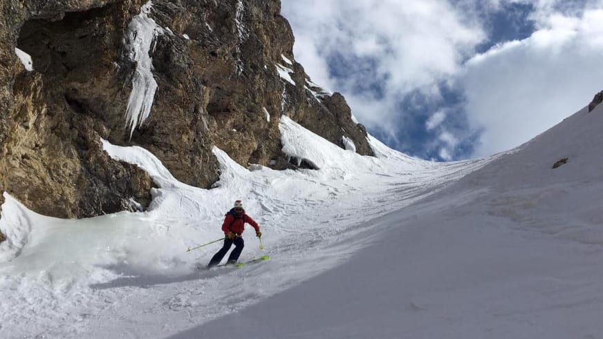 Bergführer Tommaso Cappelletto in roter Skijacke fährt mit Skiern durch verschneite Rinne zwischen Felswänden hinab.
