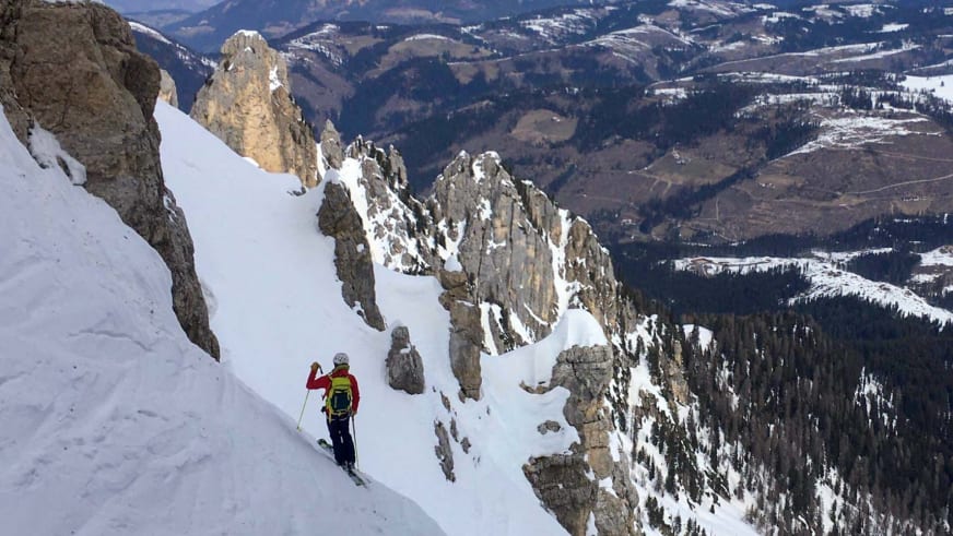 Mit roter Jacke fährt Bergführer Tommaso Cappelletto auf Skiern zwischen hohen Kalksteinfelsen einen verschneiten Hang hinab.
