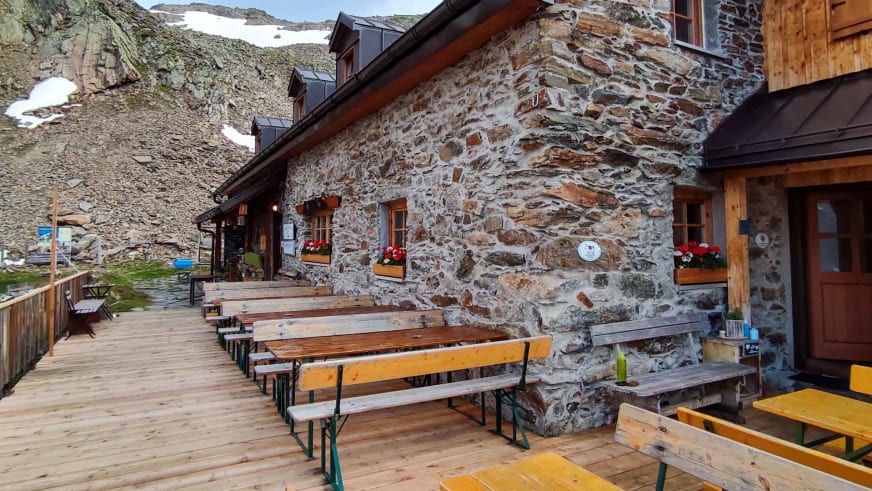 Holzterrasse der Kaunergrathütte mit Bierzeltgarnituren vor imposanter Bergkulisse.