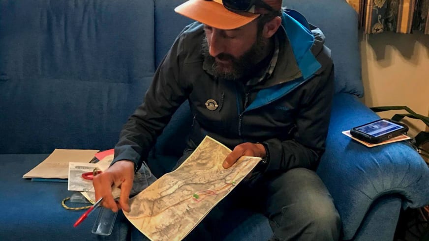 Mit oranger Mütze und rotem Stift studiert Bergführer Tommaso Cappelletto eine topographische Karte auf blauem Sessel.