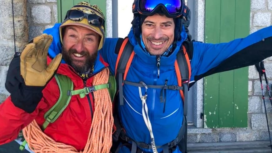Vor grünen Holzfensterläden posieren zwei Männer, darunter Bergführer Tommaso Cappelletto mit roter Jacke und Kletterseil.